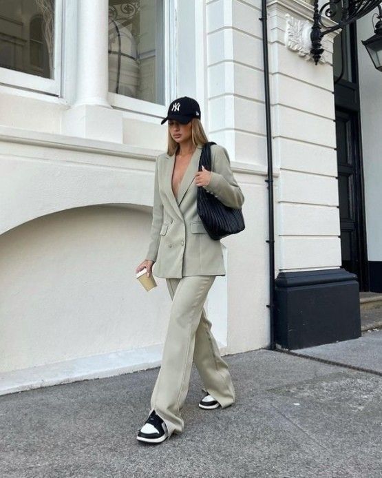 _ - 2025-06-03T122732177 Stylish woman in beige suit and cap walks by a white building, holding a black bag and a phone, urban chic fashion. | Sky Rye Design Stylish woman in beige suit and cap walks by a white building, holding a black bag and a phone, urban chic fashion.