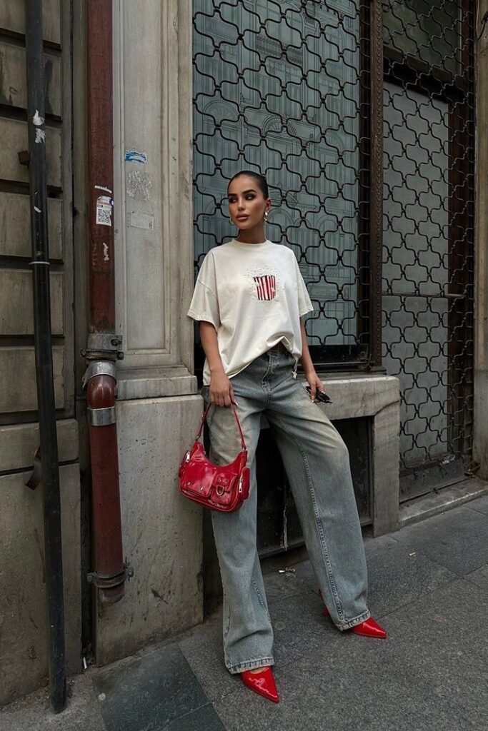 Fashion-forward woman in casual street style, wearing a white shirt and jeans with red accents, holding a matching bag.