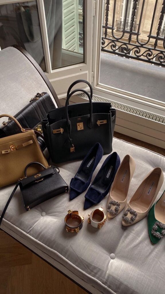 Luxury handbags, shoes, and accessories displayed on a sofa near a window with city view.