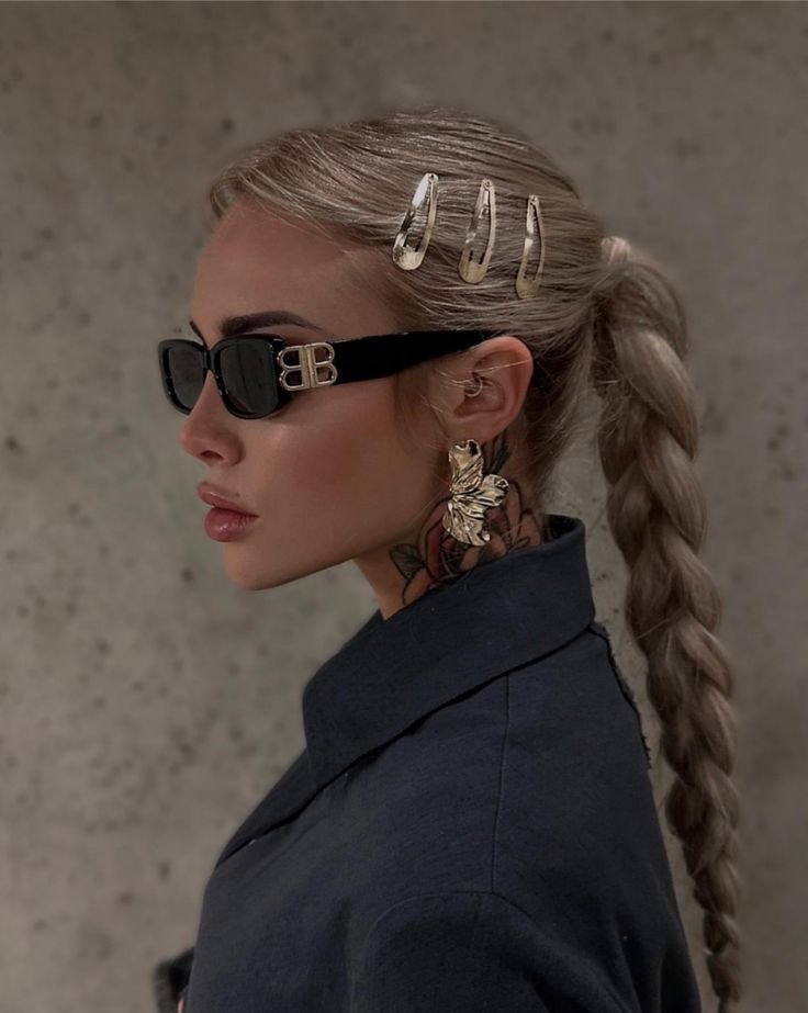 Trendy woman with braided hair, large earrings, sunglasses, and stylish hair clips on a textured background.