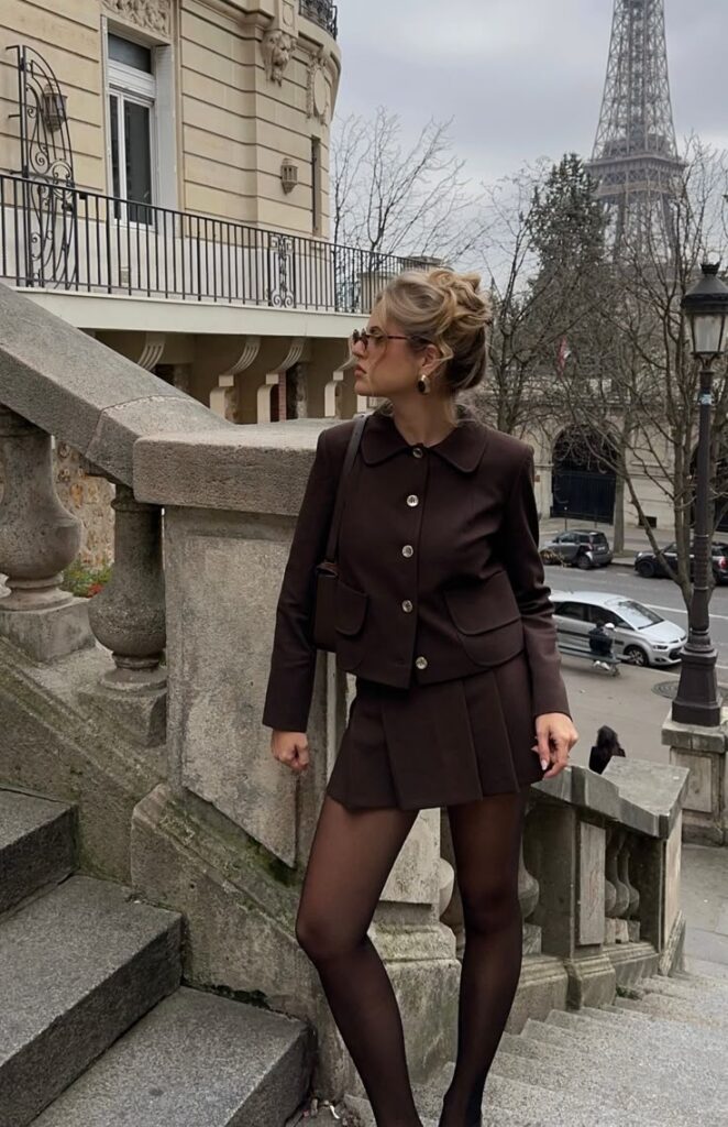 Stylish woman in brown outfit poses on Parisian steps with Eiffel Tower in background.