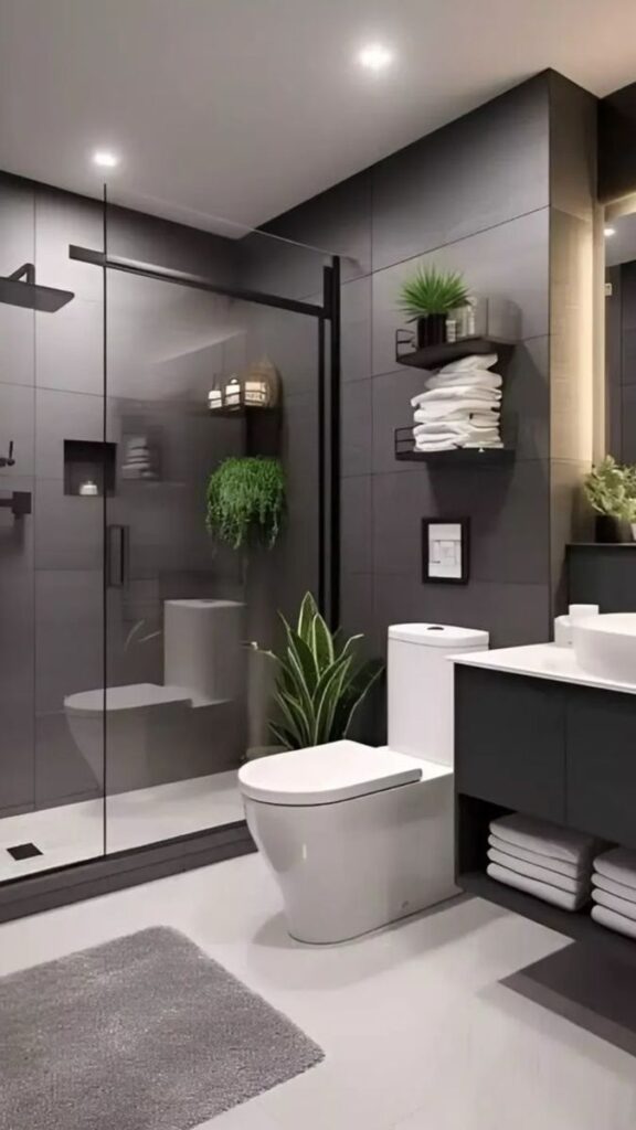 Modern bathroom with gray tiles, glass shower, plants, and sleek fixtures. Minimalist design with practical storage.