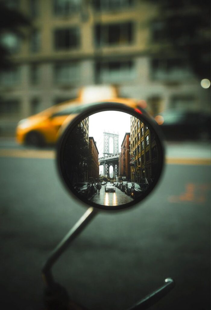 Reflection of bridge and street in car mirror with blurred city backdrop.