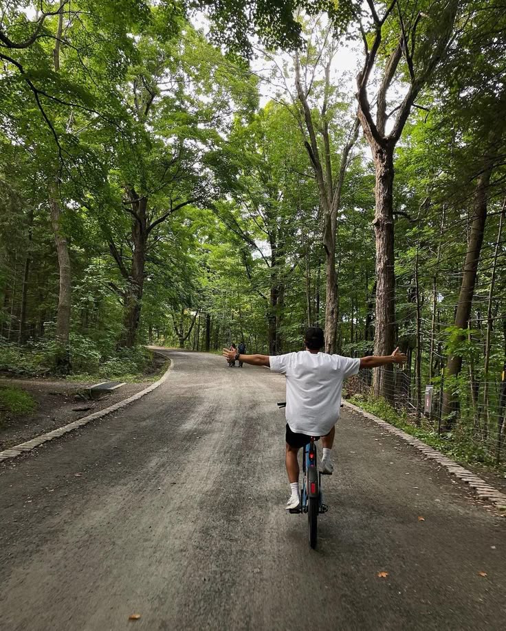 Person joyfully cycling hands-free on a forest path, surrounded by lush green trees on a summer day.