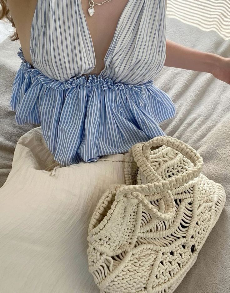 Woman in striped blue dress with crochet woven bag on bed. Fashionable, stylish summer outfit with accessories.