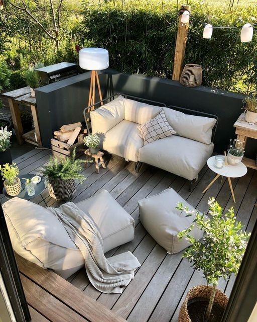 Cozy outdoor patio with white sofas, plants, and wooden flooring, perfect for relaxing and entertaining in a serene garden setting.