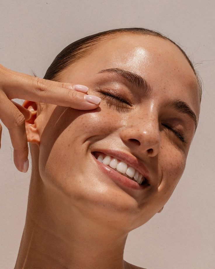 Smiling person with glowing skin, gently touching face; highlighting natural beauty and skincare.