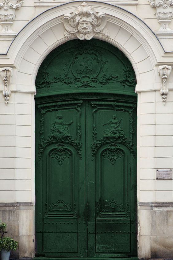 Ornate green double doors with intricate carvings beneath an arched entrance and decorative stone face.