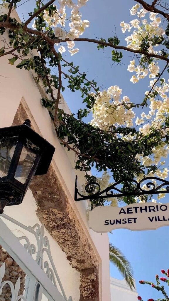 White bougainvillea and sunset villa sign against a clear blue sky, near a rustic lantern.