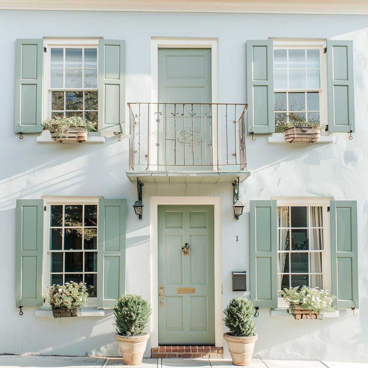 Pastel green door and shutters of charming townhouse with potted plants and balcony, exuding elegance and tranquility.