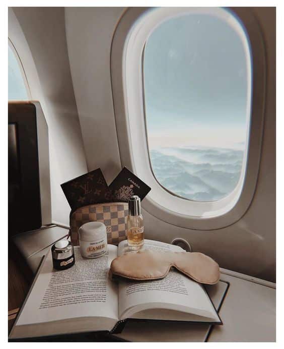 Flight luxury essentials: beauty products, eye mask, book, and a window view of clouds from an airplane. Summer makeup

