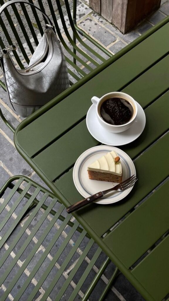 Coffee and cake on green table with metallic handbag; outdoor cafe setting.
