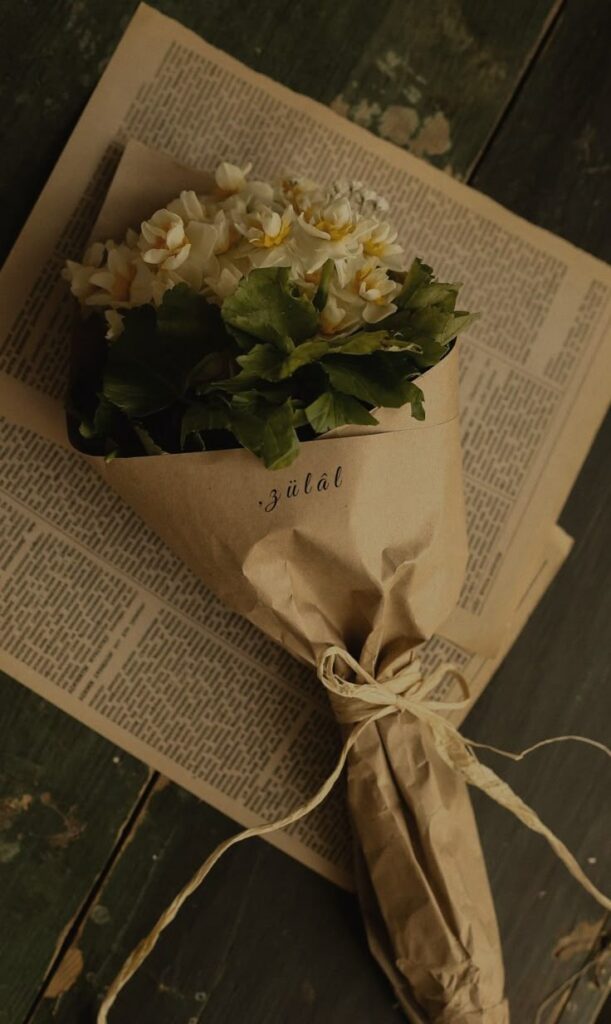 Bouquet of white flowers wrapped in brown paper placed on vintage newspapers, creating a rustic and elegant look.