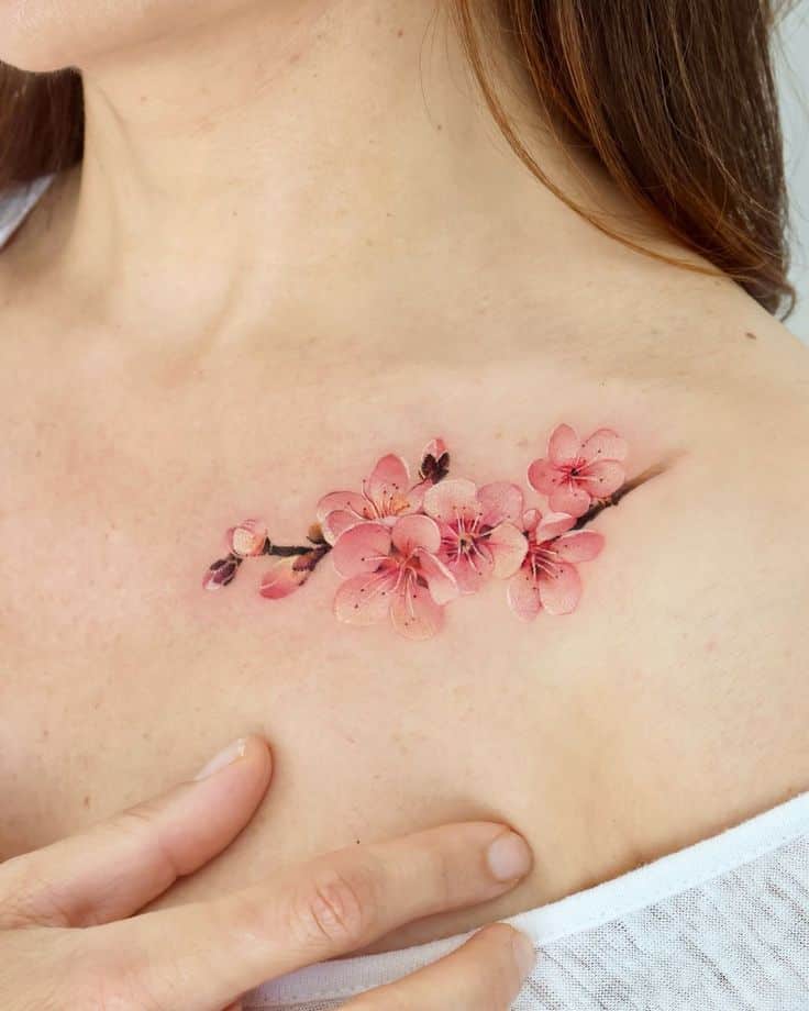 Delicate cherry blossom tattoo on collarbone, showcasing intricate pink floral design and soft shading.