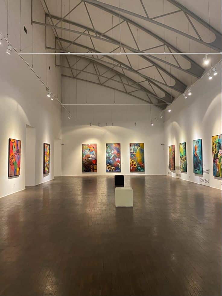 Spacious art gallery with colorful abstract paintings on white walls and high ceilings.