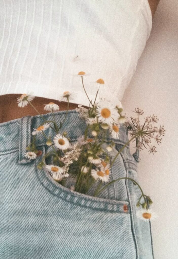 White daisies in denim pocket against a white top, emphasizing casual floral fashion and nature-inspired style.