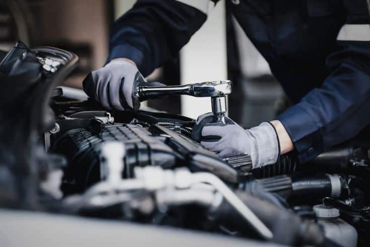 Mechanic using wrench for car engine repair, wearing gloves. Automotive maintenance in a workshop setting.