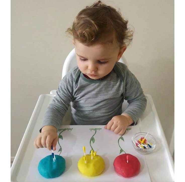 Toddler playing with colorful playdough and pegs; early learning activity at high chair.