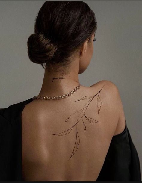_ 26 Back view of a woman with a minimalistic leaf tattoo on shoulder, wearing a gold chain and black draped jacket. | Sky Rye Design Back view of a woman with a minimalistic leaf tattoo on shoulder, wearing a gold chain and black draped jacket.