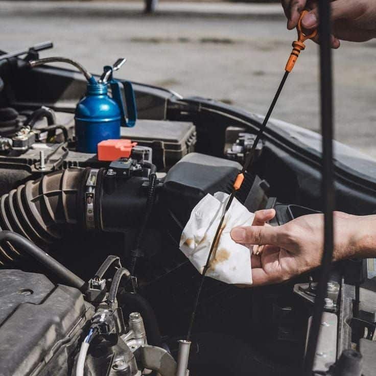 Checking car engine oil level with dipstick, close-up of hand holding dipstick and paper towel.