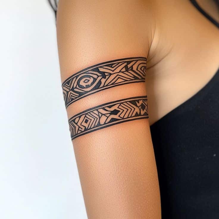 Intricate tribal band tattoo design on a woman's upper arm, featuring geometric patterns and fine line details.