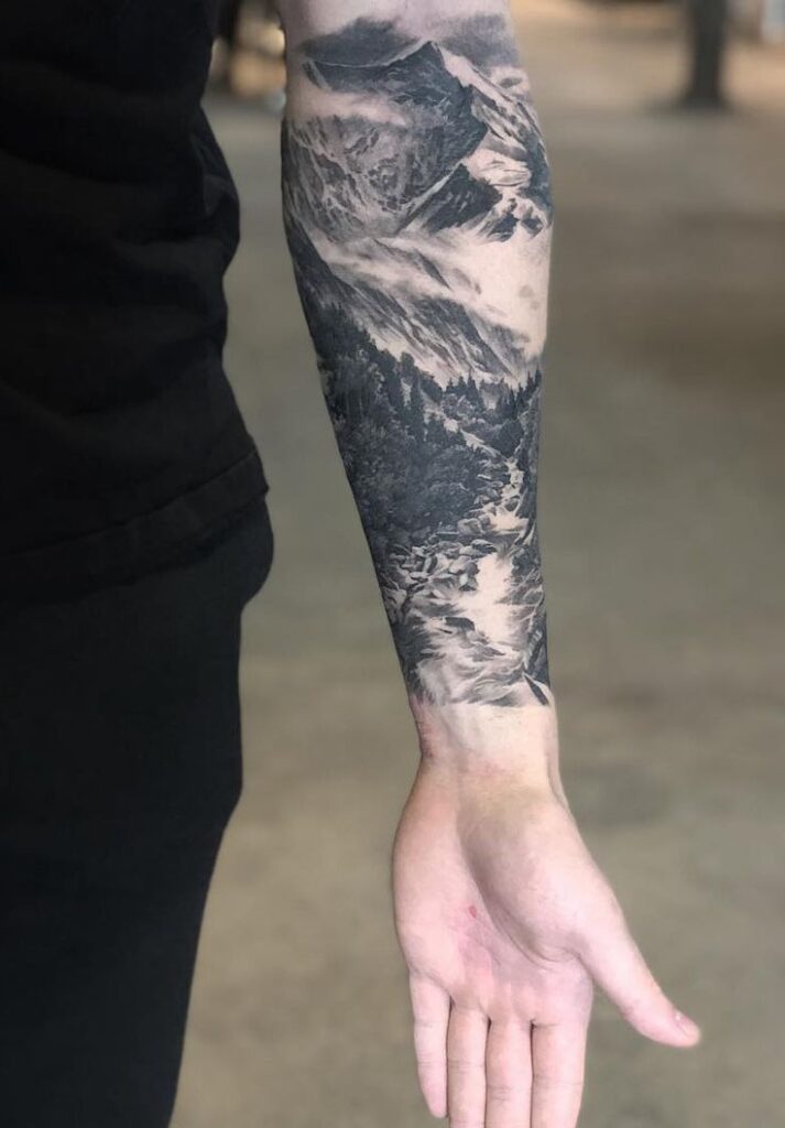 Arm with detailed scenic mountain landscape tattoo in black and gray.