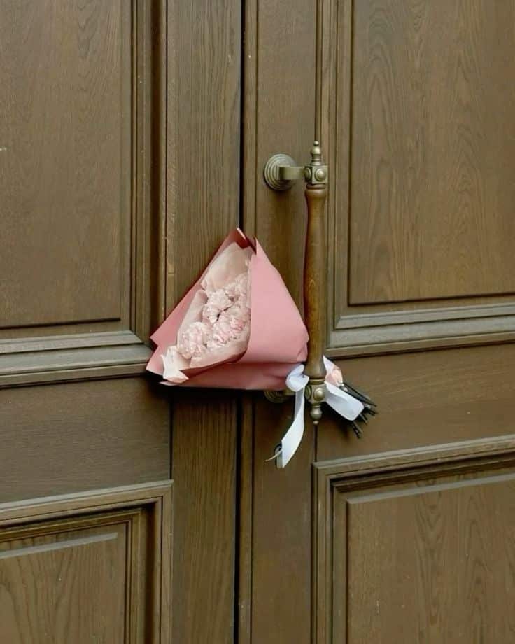 Pink bouquet hanging on ornate wooden door handle, accentuating elegance and surprise.