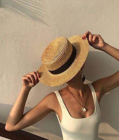 Woman in white tank top holding a wide-brimmed straw hat, casting a shadow on a sunny day. Summer style.