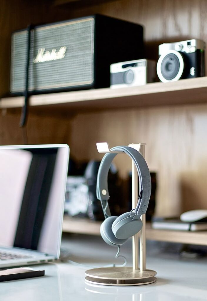 Modern workspace with headphones, vintage camera, speaker, and laptop on a desk.