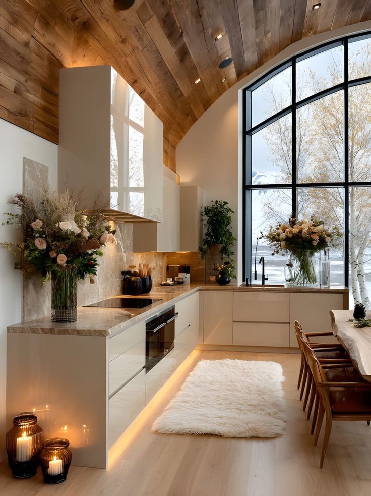 Luxurious kitchen with vaulted wood ceiling, large window, modern cabinets, and elegant decor for a cozy ambiance.