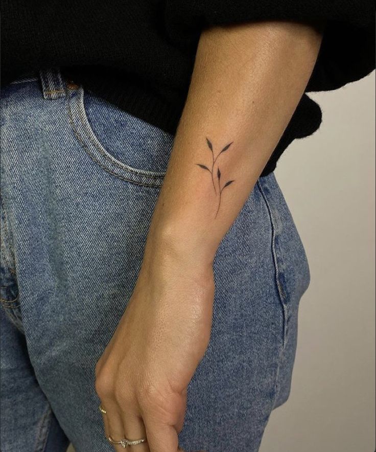 Minimalistic plant tattoo on forearm, hand in jeans pocket. Minimalist tattoo art, nature-inspired design.