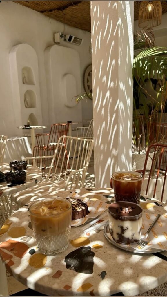 2ac2842f-1bab-4e9f-967d-54300a0270ec Cozy cafe setting with iced coffees, desserts, and dappled light on terrazzo tables and white chairs. | Sky Rye Design Cozy cafe setting with iced coffees, desserts, and dappled light on terrazzo tables and white chairs.