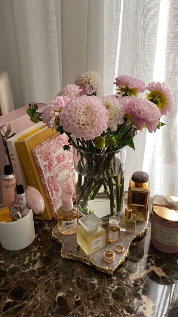 2b0e7611-35fe-47d5-85ea-64678e7c32a8 Pink flowers in vase on marble table with perfume, books, and candles, creating a cozy, elegant atmosphere. | Sky Rye Design Pink flowers in vase on marble table with perfume, books, and candles, creating a cozy, elegant atmosphere.