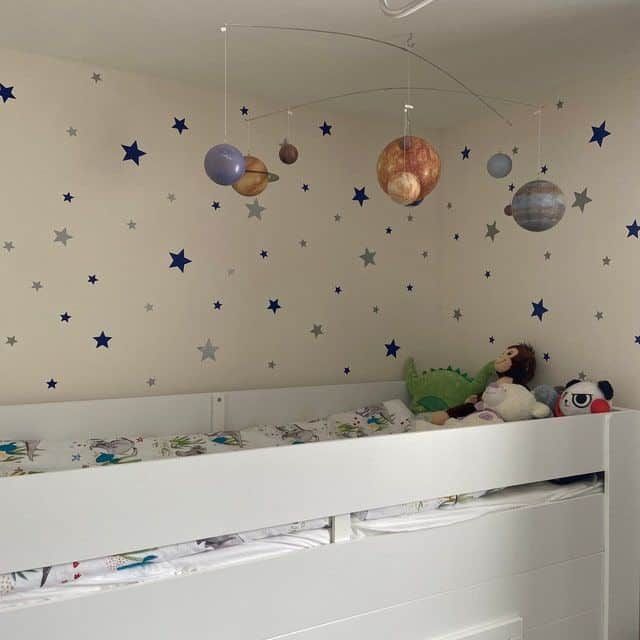 Kids' room with star decals, a solar system mobile, and a cozy bed with stuffed animals. Perfect for a space-themed decor.