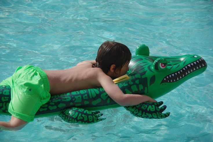Child enjoying pool on inflatable green alligator float.