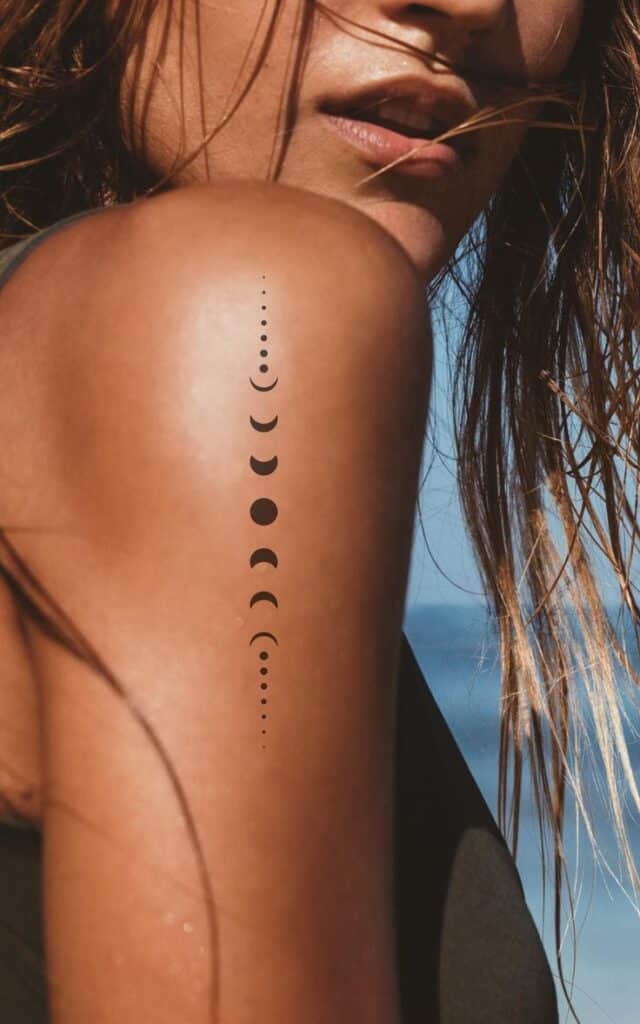 Woman with moon phase tattoo on shoulder, beach background, close-up.
