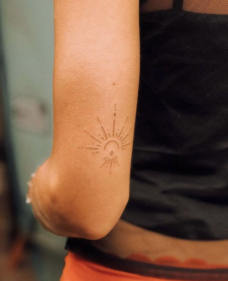 Minimalist sunburst tattoo on arm, featuring crescent and rays design.