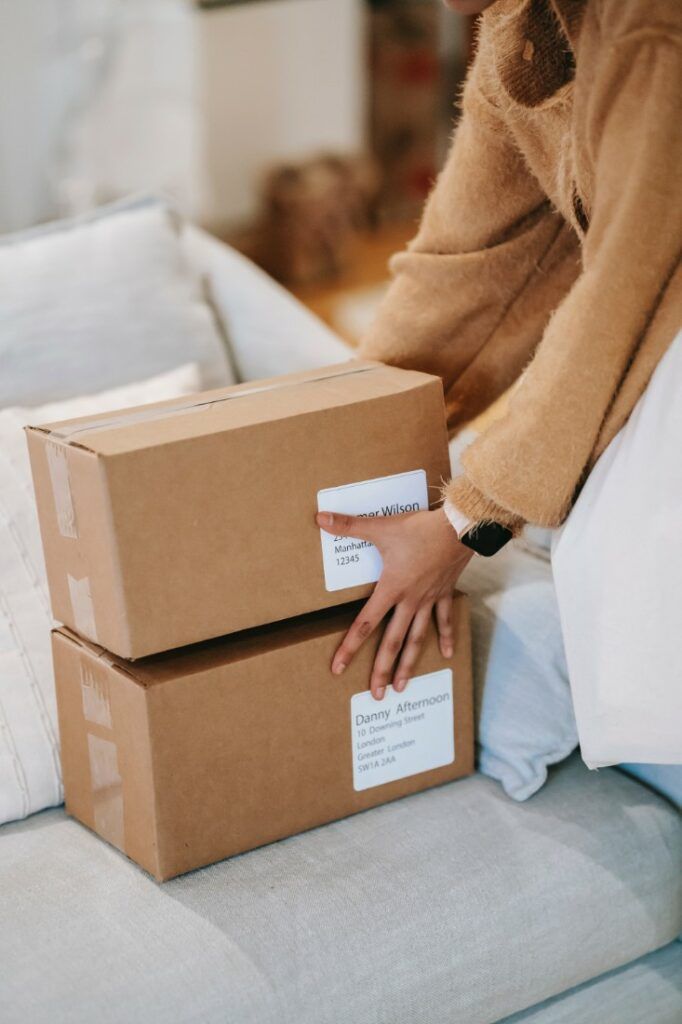 Person placing labeled cardboard boxes on couch, indicating home delivery or packaging service.