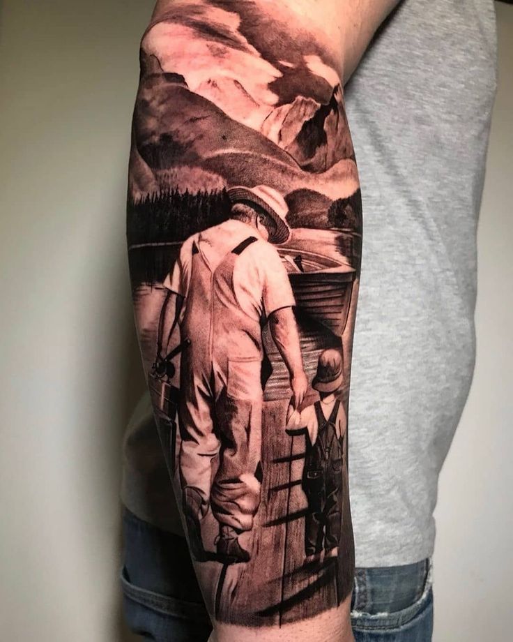 Forearm tattoo of an adult and child walking on a pier, with a scenic mountain and lake backdrop in grayscale.