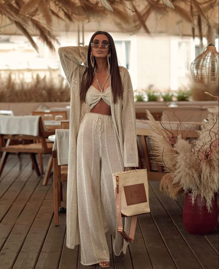 Woman in stylish crochet outfit and sunglasses posing in a boho-chic restaurant setting.