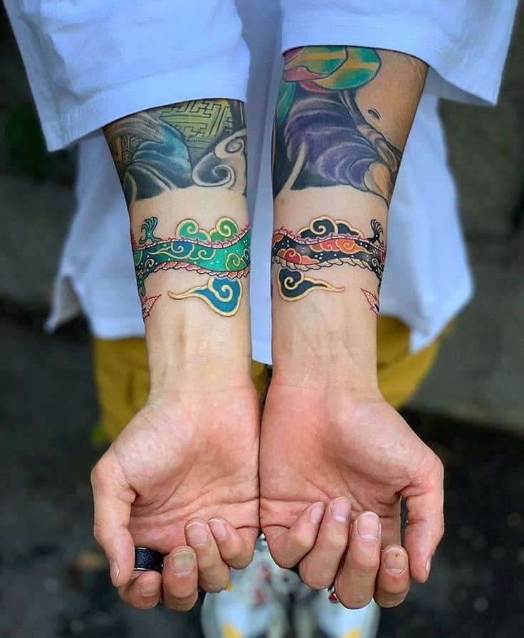 Colorful dragon tattoos encircling both wrists with vibrant details.