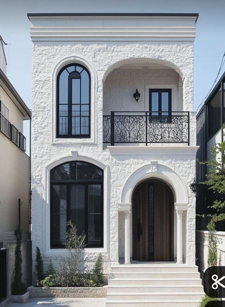 Elegant white stone house with arched windows, a decorative balcony, and a stylish wooden door.