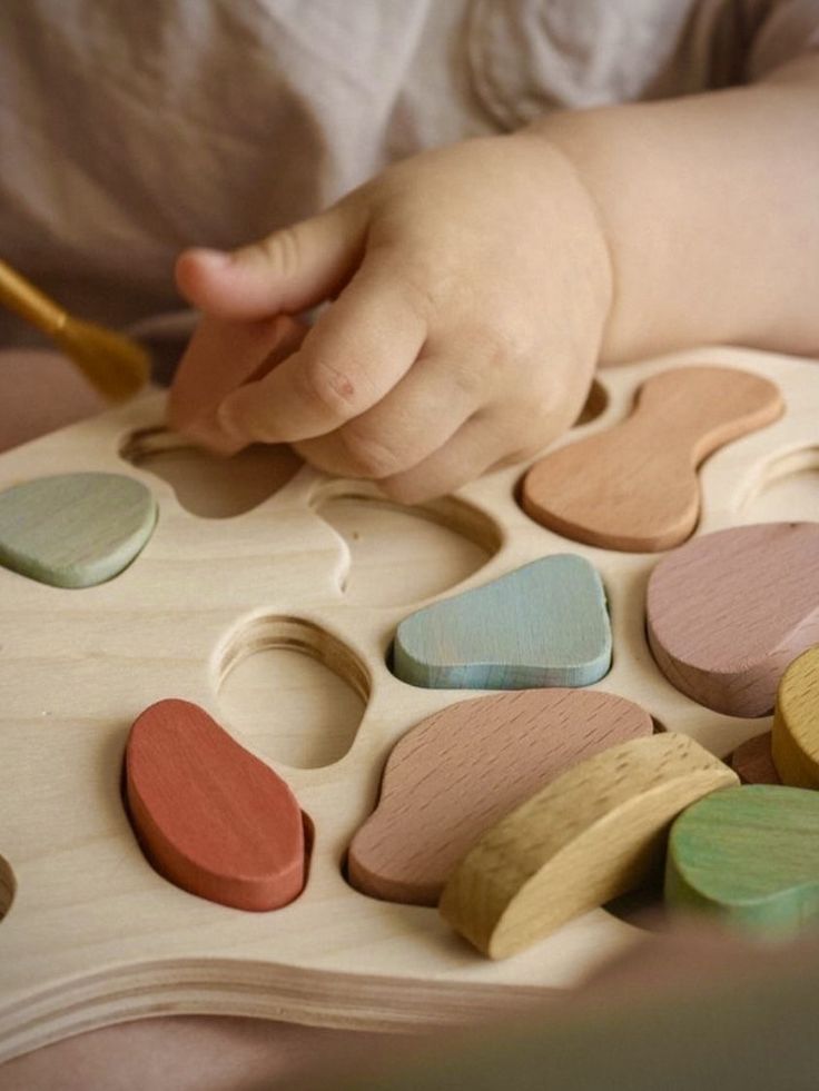 Child's hand playing with colorful wooden puzzle pieces on a light wooden board.