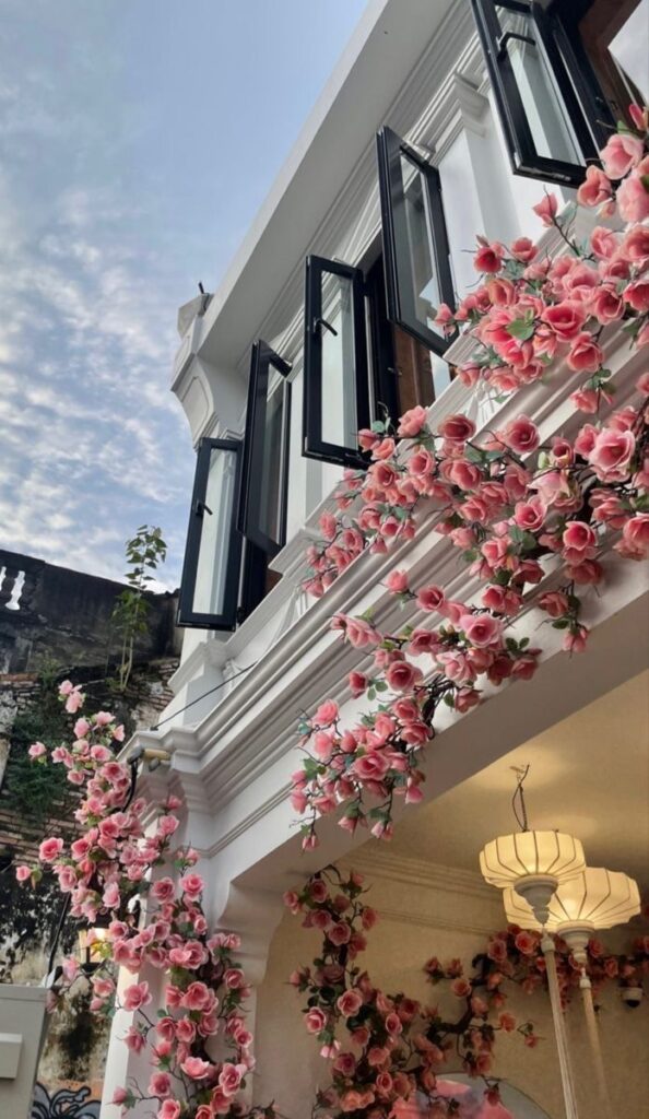 Elegant building with open windows, adorned with pink floral vines under a partly cloudy sky. Flower Wallpaper iPhone