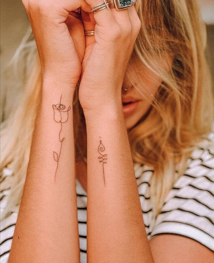 Minimalist line tattoos on forearms, featuring a rose and abstract design, with a striped shirt in the background.