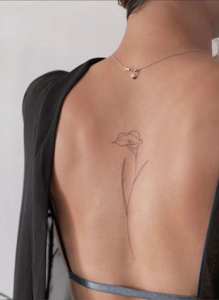 Minimalist flower tattoo on a woman's back with open-back top, showcasing delicate line art style.