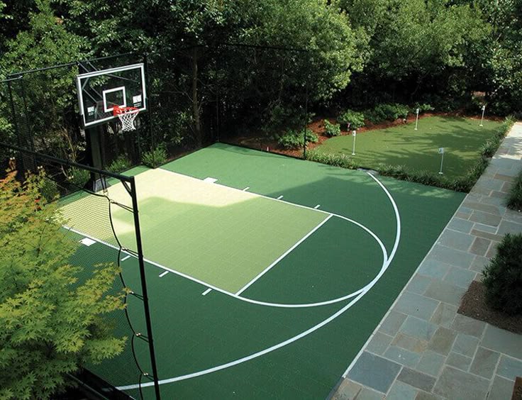 Backyard sports court with basketball hoop and putting green, surrounded by greenery and paved walkway.