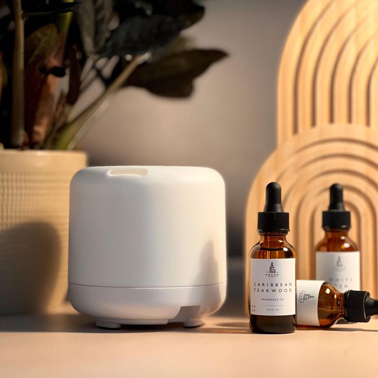 White essential oil diffuser with Caribbean Teakwood fragrance bottles on a stylish tabletop setting.