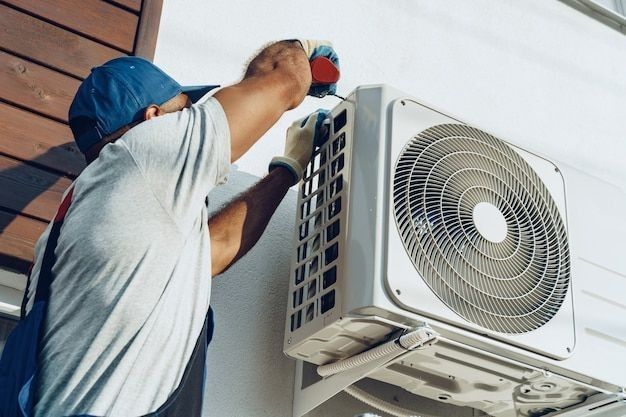 Technician servicing outdoor air conditioning unit on building wall.