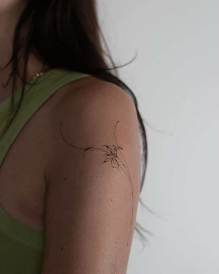 Minimalist floral tattoo on a woman's shoulder in a green top.